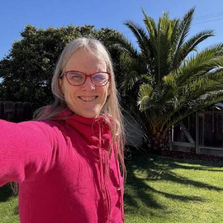 A picture of Brooke smiling, standing in the sun with a palm tree in the background.